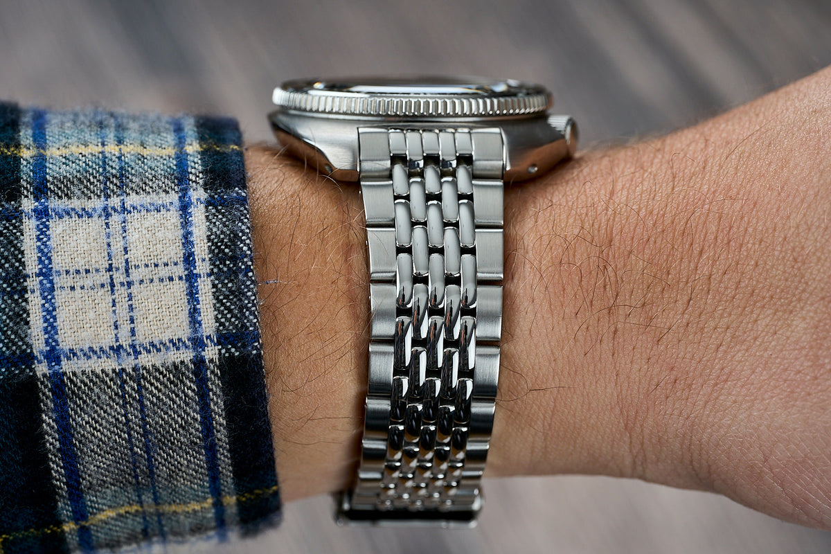 Stainless steel beads of rice bracelet watch on wrist with blue plaid shirt cuff, showing linked metal band detail