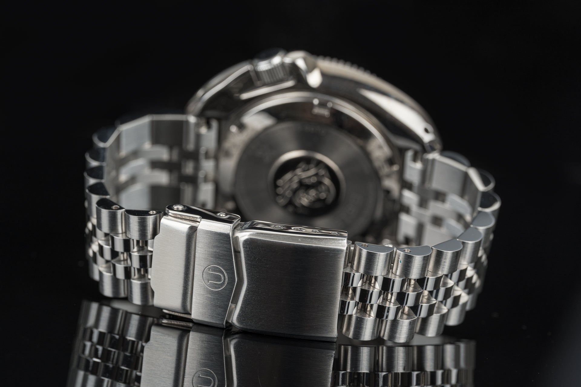 Stainless steel automatic dive watch with metal bracelet and fold-over safety clasp, shown from front and back views against black background
