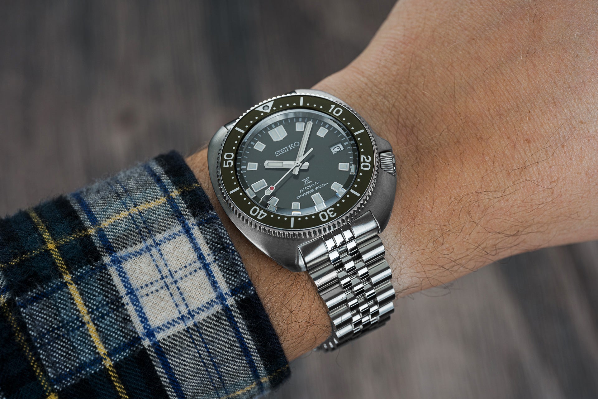 Seiko Prospex automatic dive watch with black dial, stainless steel bracelet and rotating bezel on wrist with plaid sleeve