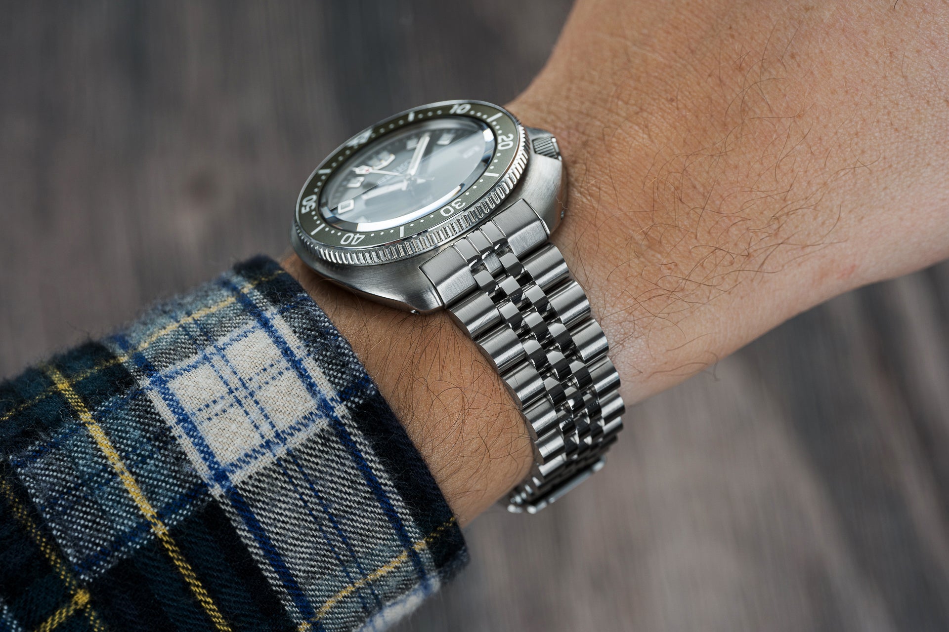 Stainless steel dive watch with rotating bezel and jubilee bracelet worn on wrist with plaid shirt