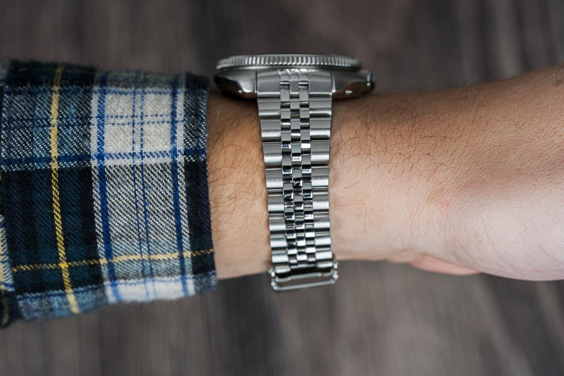 Stainless steel bracelet watch worn on wrist with plaid shirt sleeve, showcasing jubilee link band and round dial