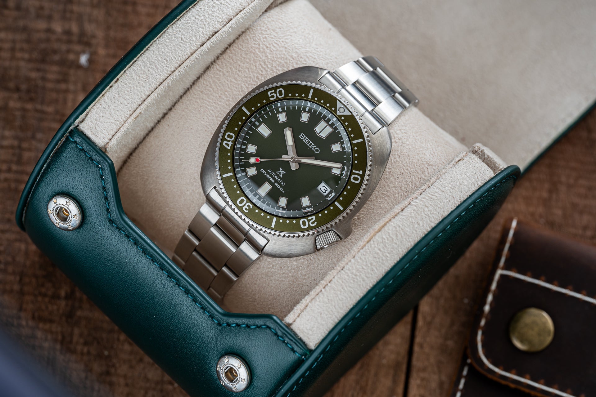 Seiko Prospex automatic dive watch with black dial and olive bezel on steel bracelet displayed in teal leather watch roll