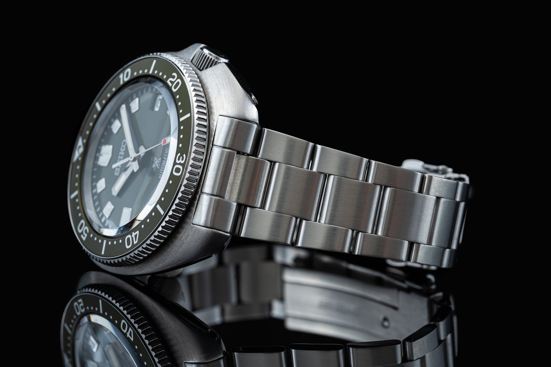 Stainless steel dive watch with black dial, rotating bezel, and matching metal bracelet on reflective black surface