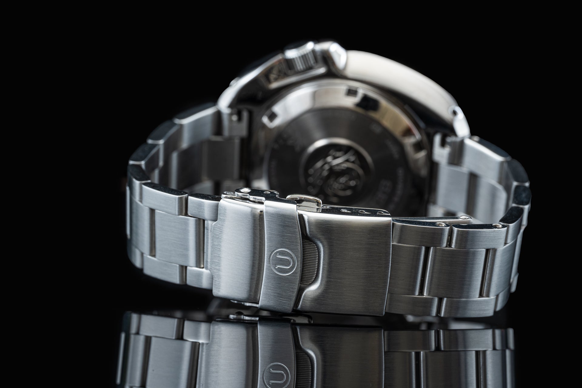 Stainless steel dive watch with metal bracelet and fold-over clasp, shown from side view against black background