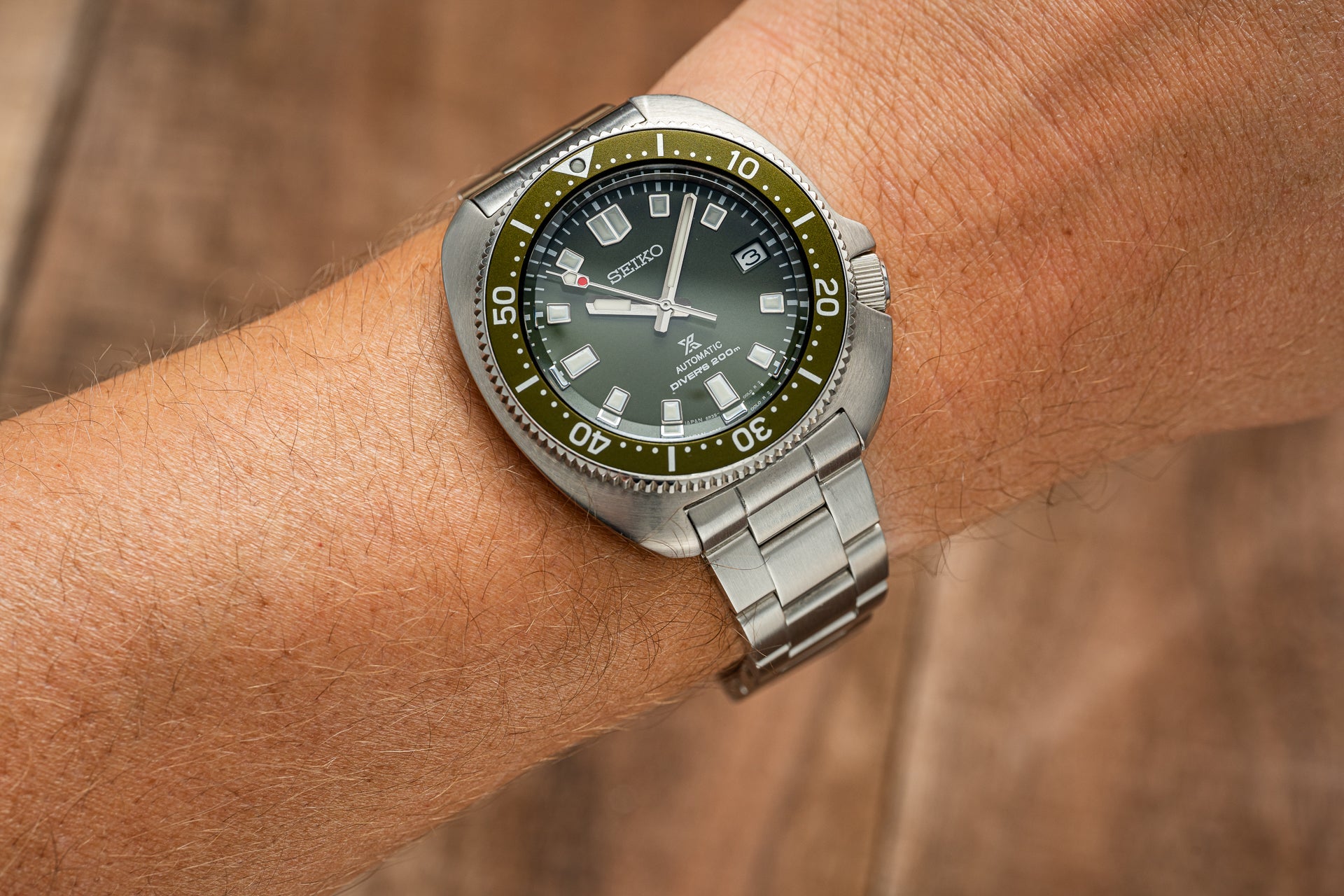 Seiko Prospex automatic dive watch with dark green dial, olive bezel, and stainless steel bracelet worn on wrist