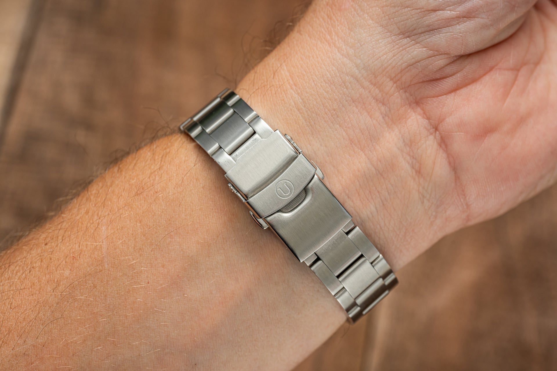 Stainless steel watch bracelet with solid links and deployment clasp worn on wrist, featuring brushed and polished finish