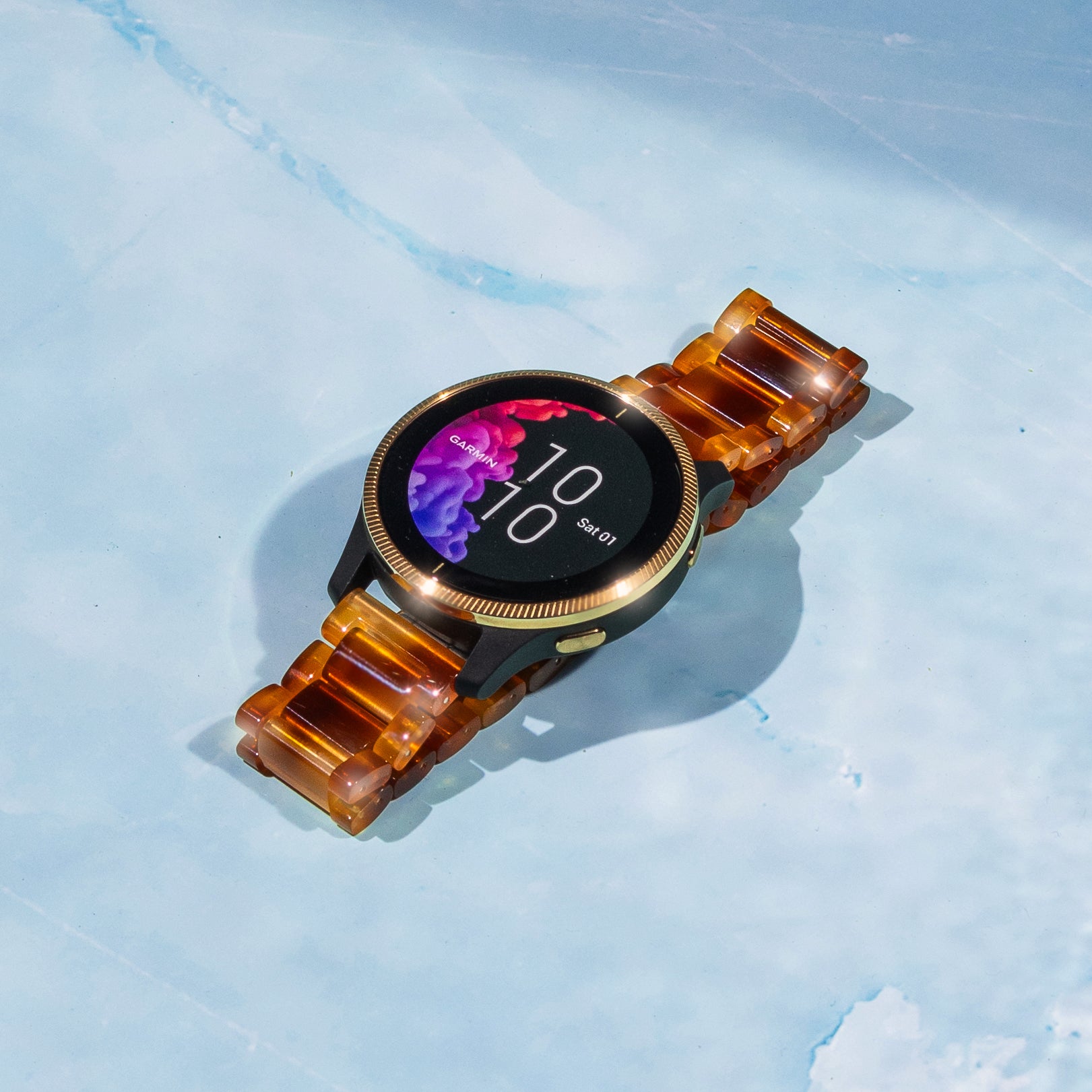 Garmin smartwatch with tortoiseshell brown acetate band and gold bezel displaying time on black AMOLED screen