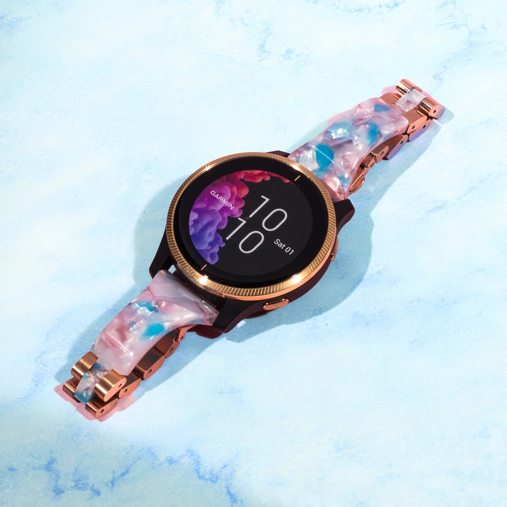 Rose gold smartwatch with pink acetate bangle strap and colorful digital display on light blue background