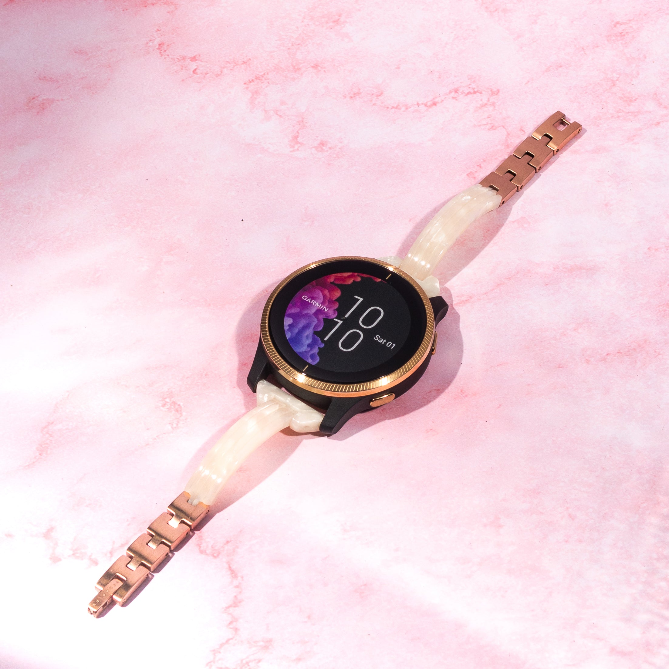 Garmin smartwatch with white pearl acetate quick release band and rose gold hardware on pink textured background