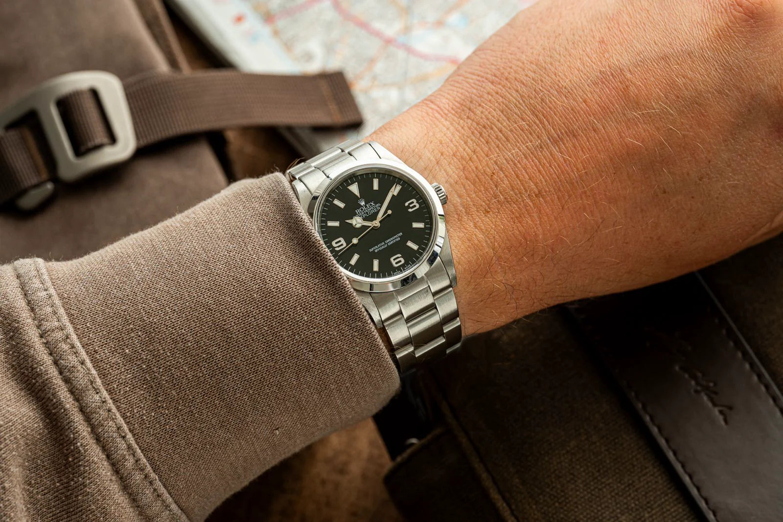 Stainless steel luxury watch with black dial on wrist, paired with brown fabric strap and map background