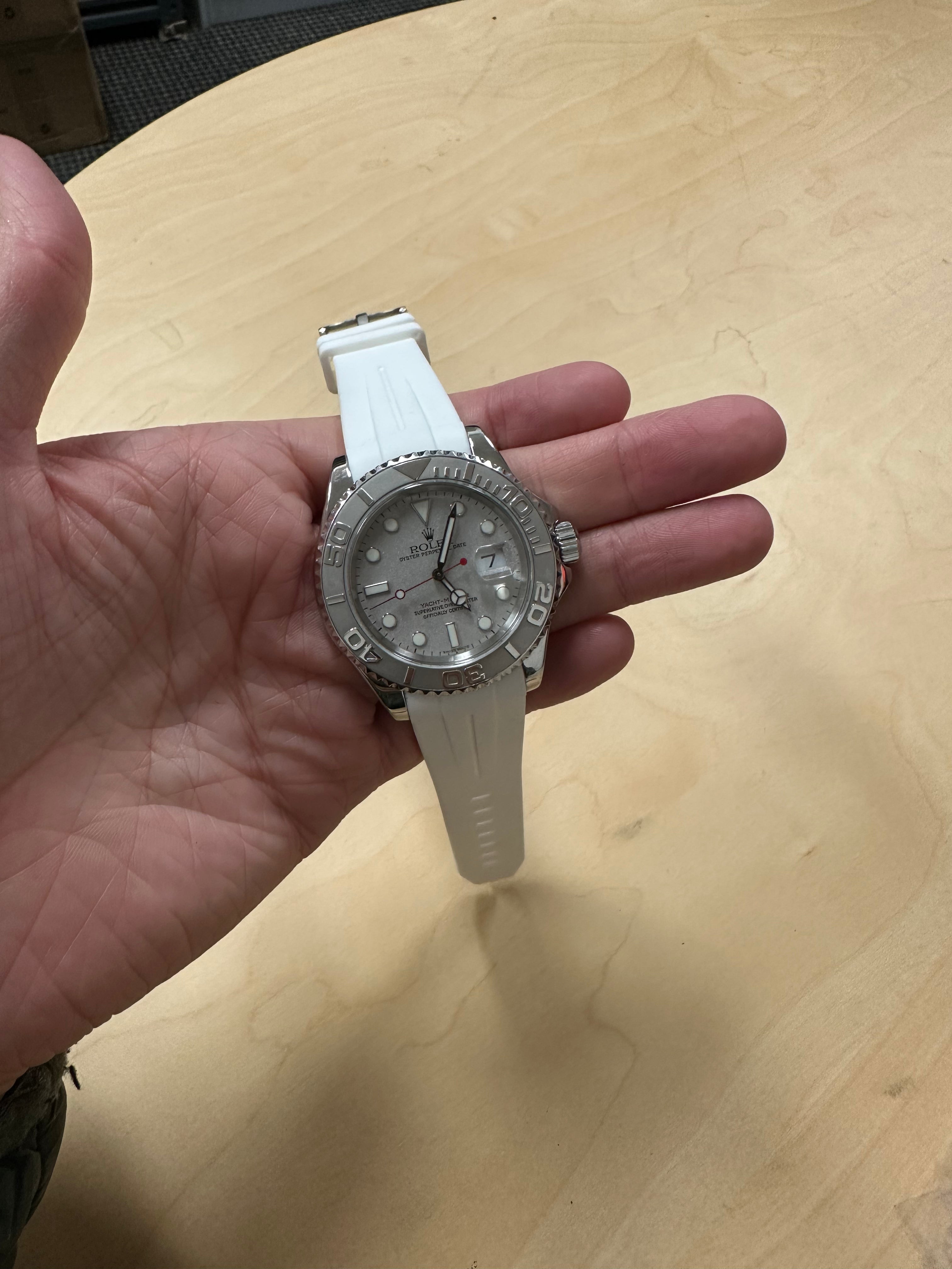 Luxury sports watch with silver dial and white rubber strap held in hand on wooden surface