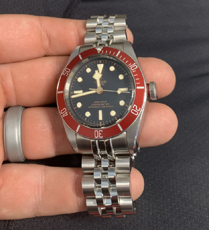 Stainless steel jubilee bracelet with solid links fitted on vintage Tudor Black Bay dive watch with red bezel and black dial held in hand