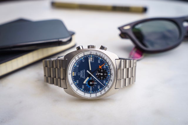 Vintage Omega Seamaster chronograph watch with blue dial and steel bracelet on white desk with sunglasses