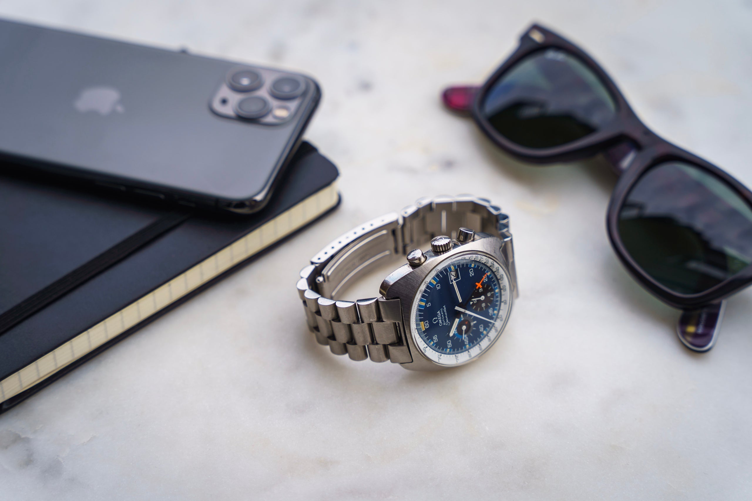 Luxury chronograph watch with blue dial and steel bracelet displayed with smartphone and sunglasses