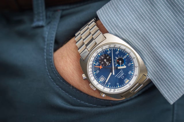Stainless steel chronograph watch with blue dial and metal bracelet on wrist wearing business shirt