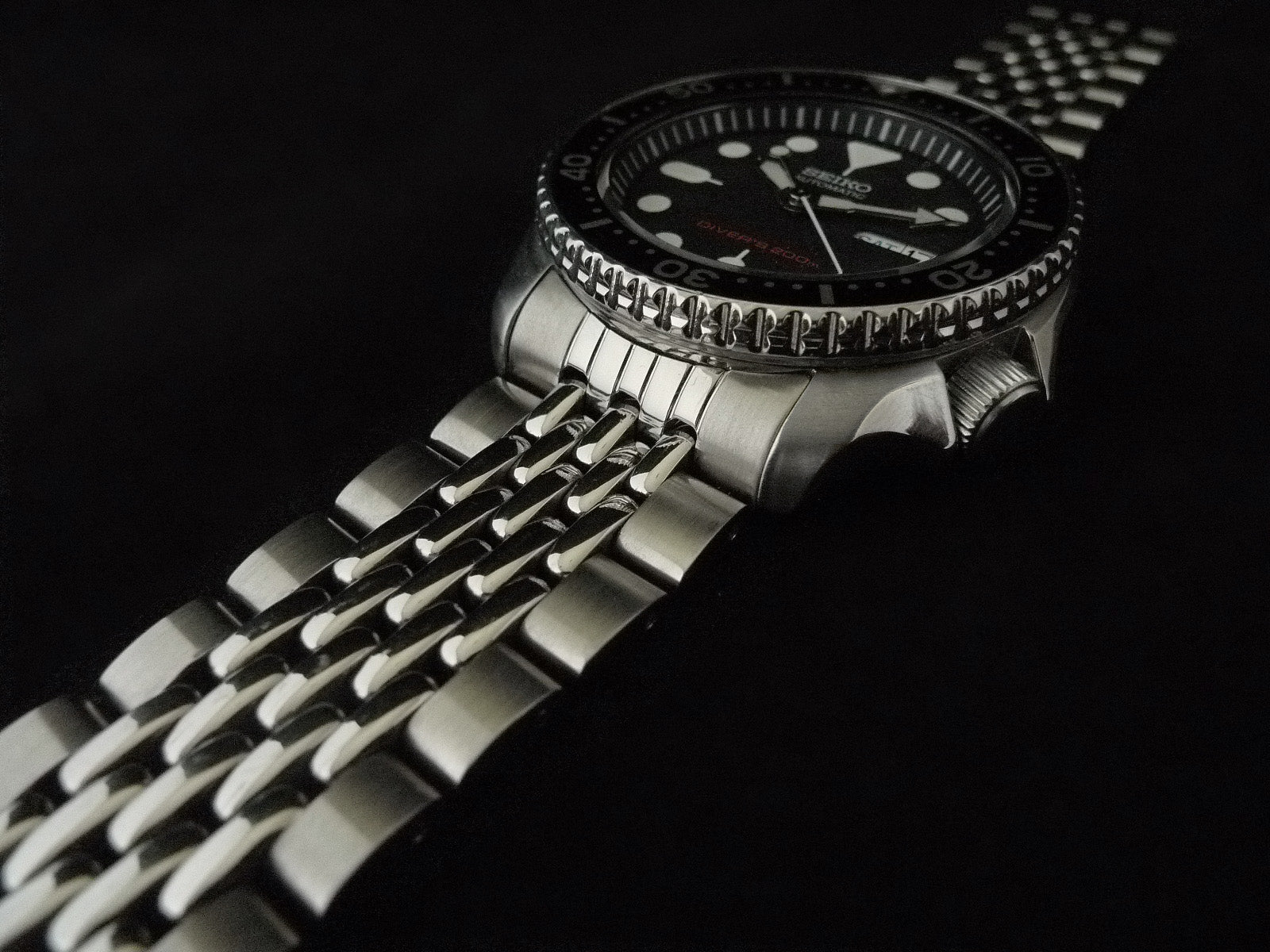 Black dial diving watch with stainless steel beads of rice bracelet on dark background, showing luminous markers and rotating bezel