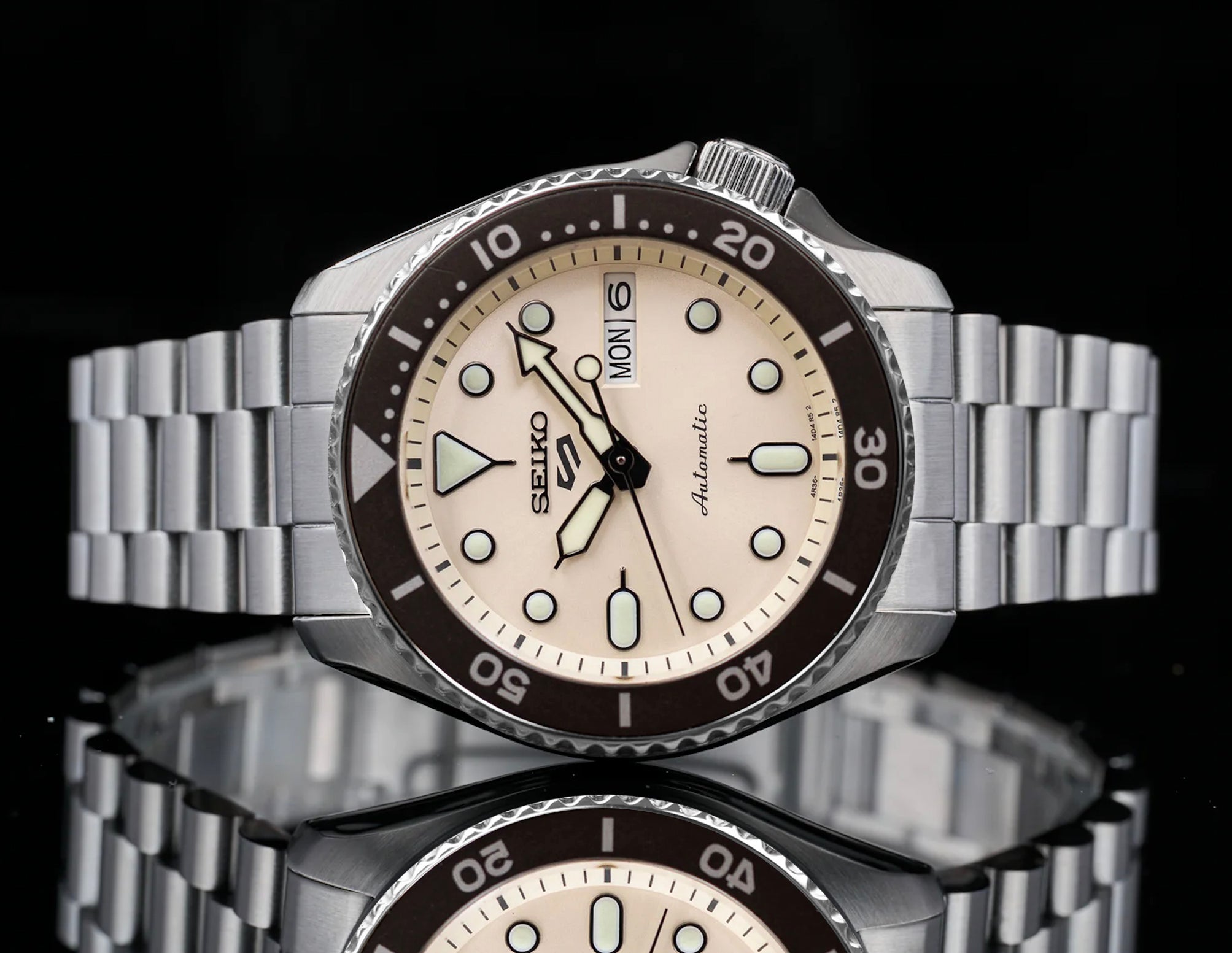 Seiko 5 Sports automatic stainless steel watch with cream dial, black bezel, and metal bracelet