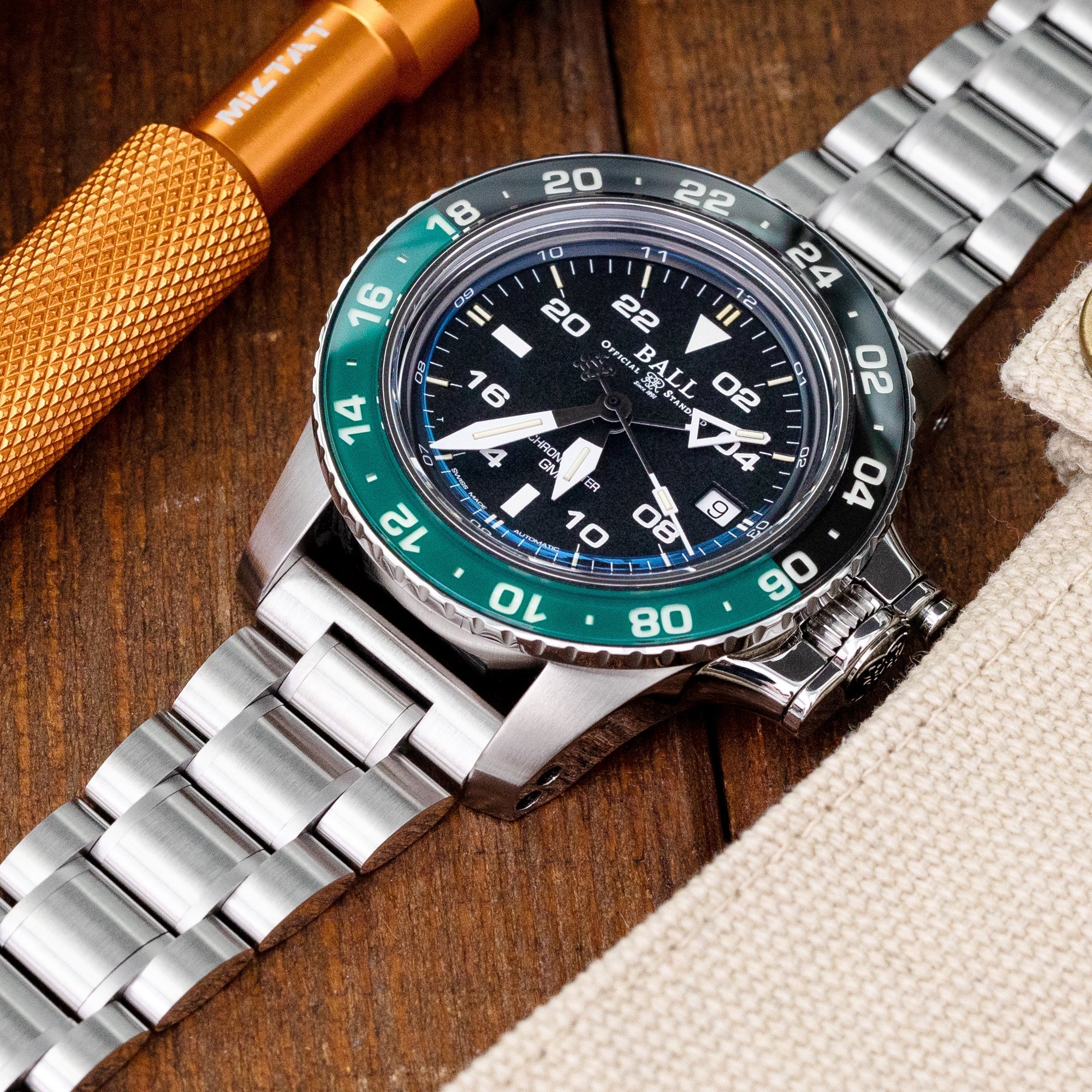 Stainless steel bracelet with V-clasp clasp displayed next to luxury sports watch on wooden surface