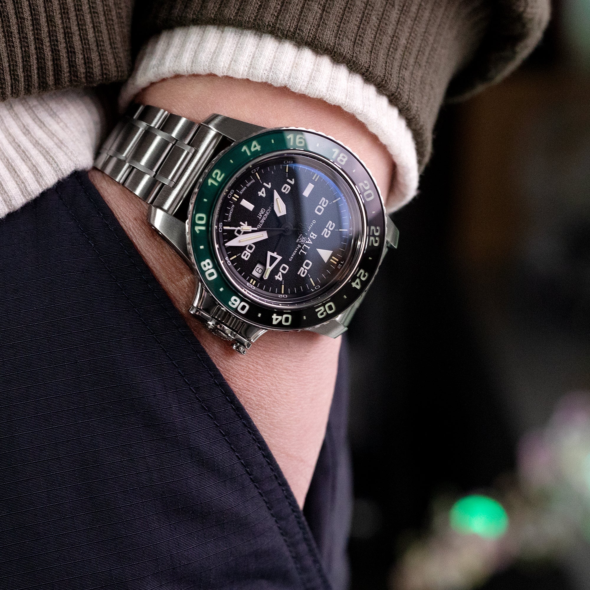 Men's stainless steel sports watch with black dial and green bezel on metal bracelet worn on wrist