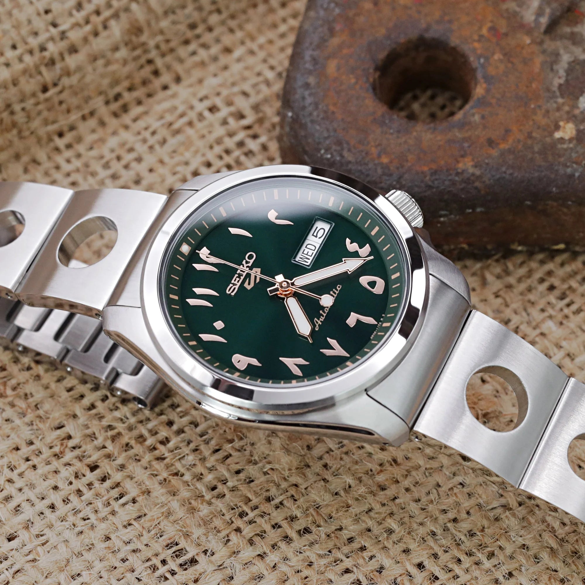 Seiko 5 Sports 40mm watch with green dial and stainless steel Rollball bracelet on beige fabric background