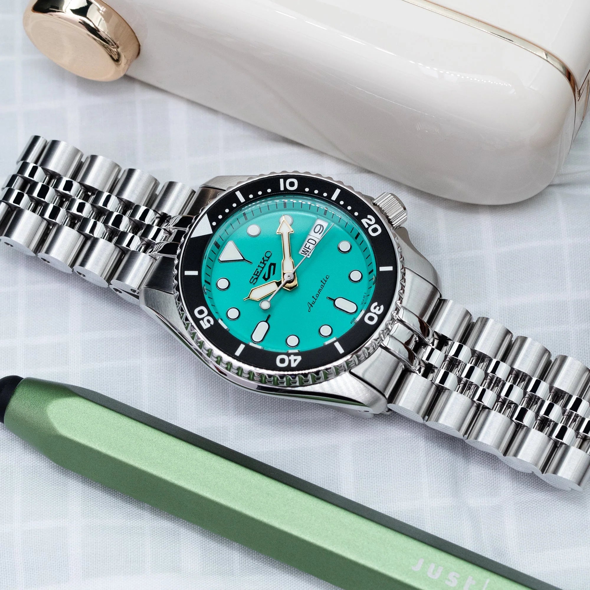 Seiko 5 Sports 38mm watch with turquoise dial and stainless steel Super-J Louis bracelet, displayed with accessories