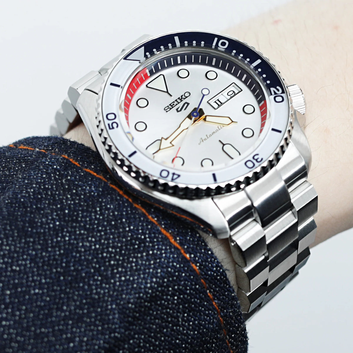 Seiko 5 automatic watch with white dial and red bezel on stainless steel Hexad bracelet