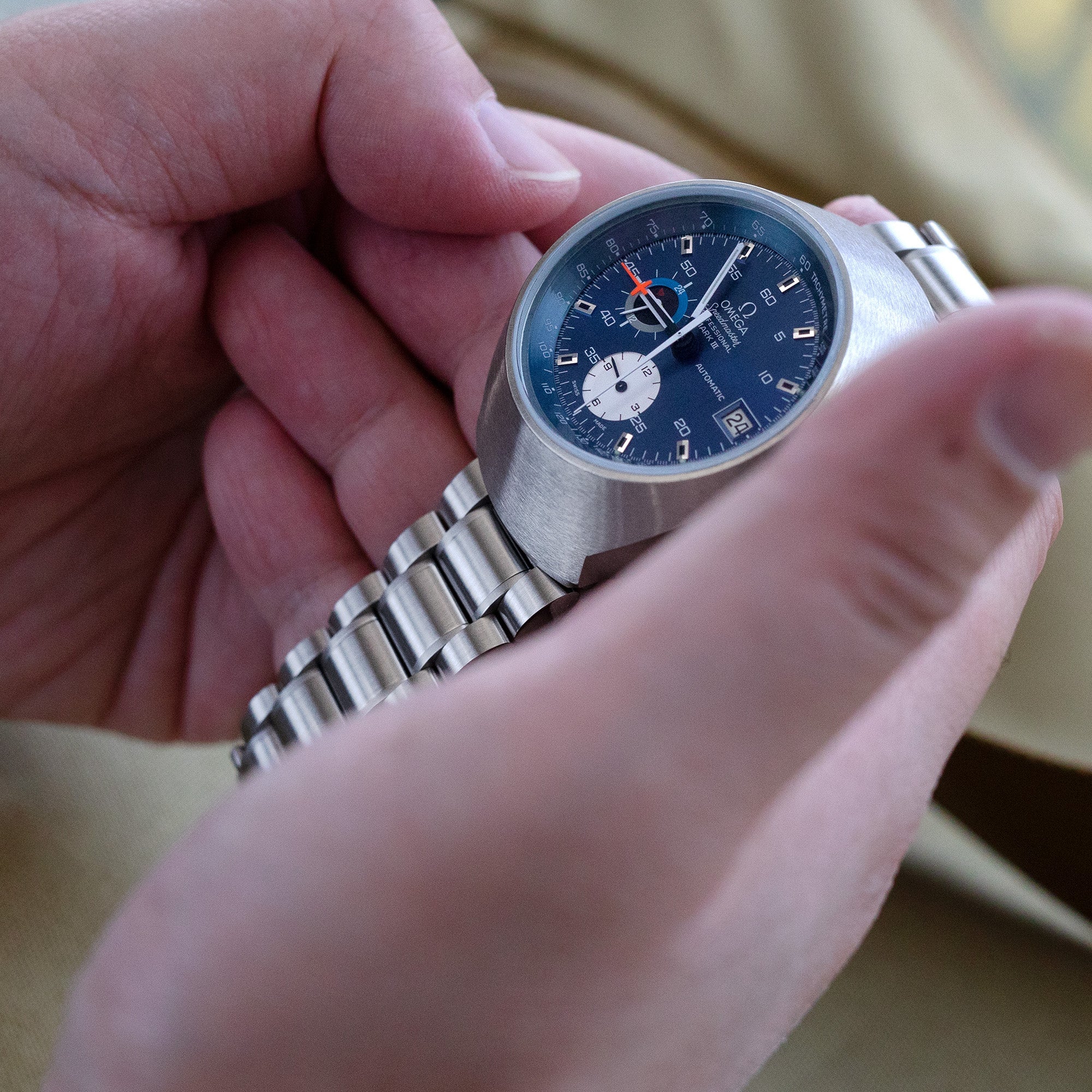 Stainless steel chronograph watch with blue dial and white subdials held in hand, featuring metal bracelet with V-clasp