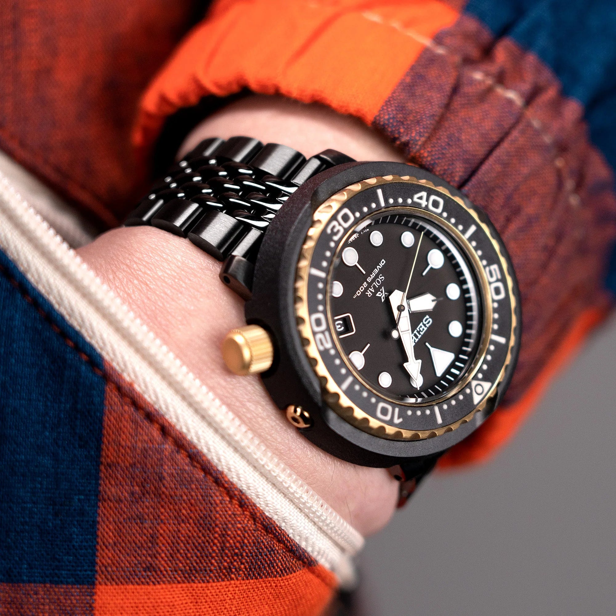 Black DLC coated stainless steel Goma BOR watch bracelet with V-clasp on wrist wearing orange jacket