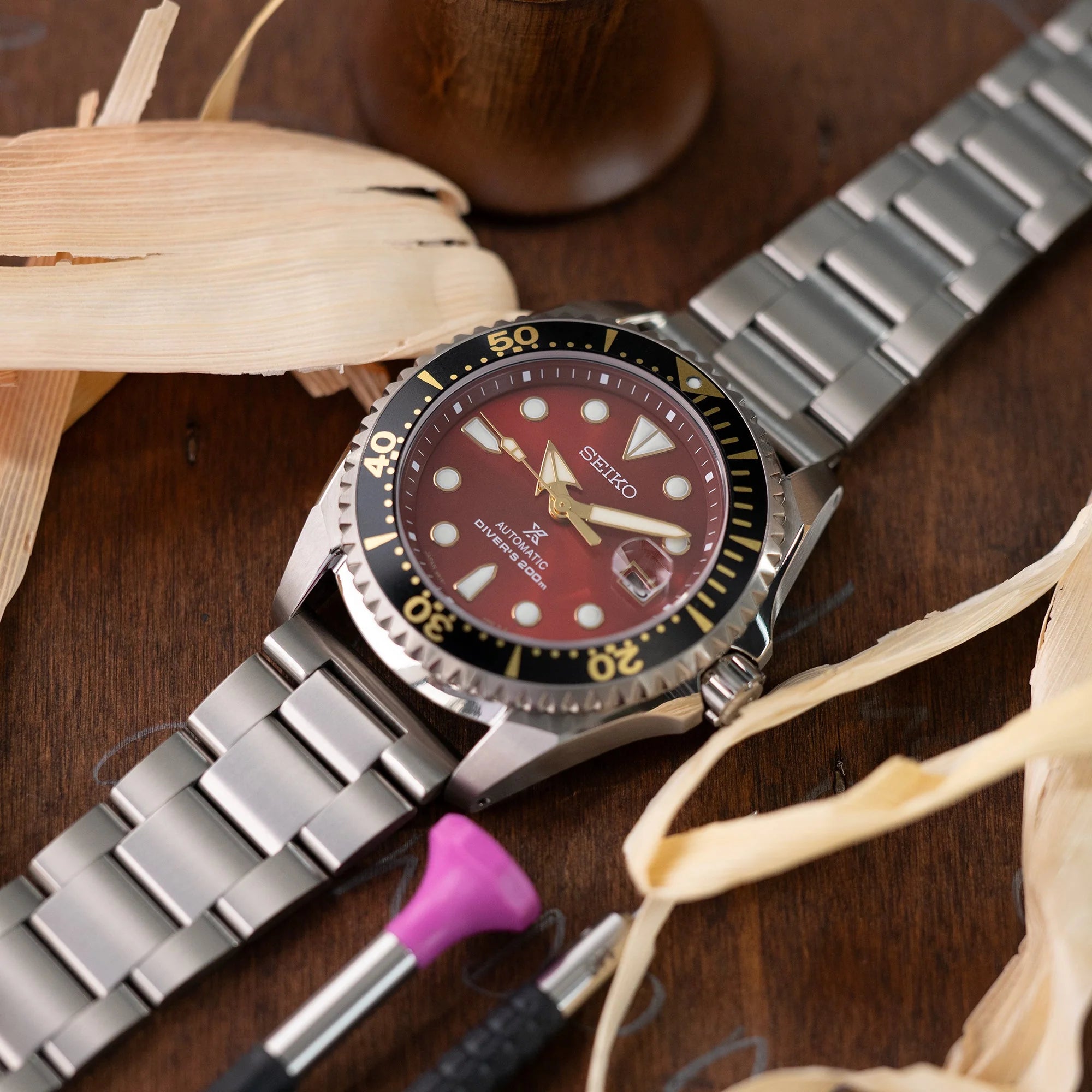 Seiko automatic dive watch with burgundy dial and steel bracelet displayed on wooden surface with watch tools