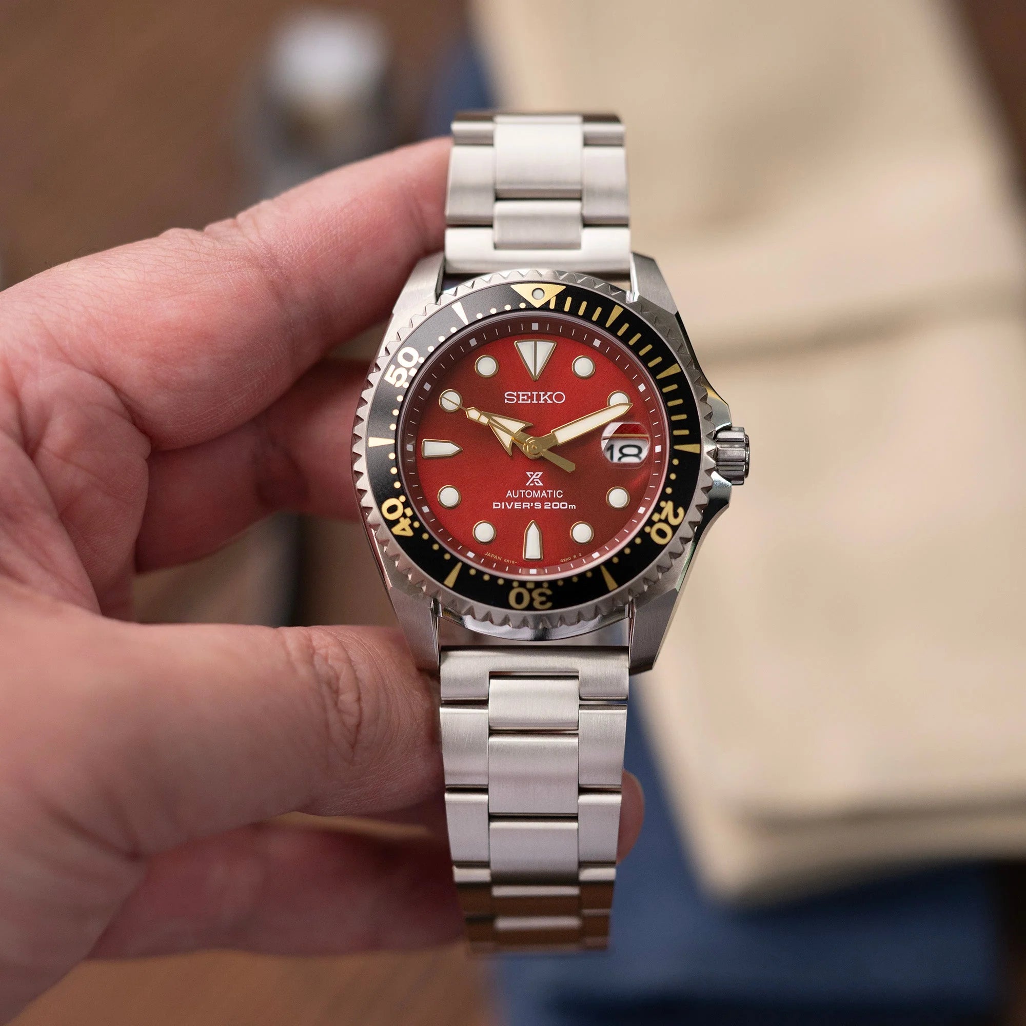 Seiko automatic diver's watch with red dial, stainless steel bracelet, black and gold bezel held in hand