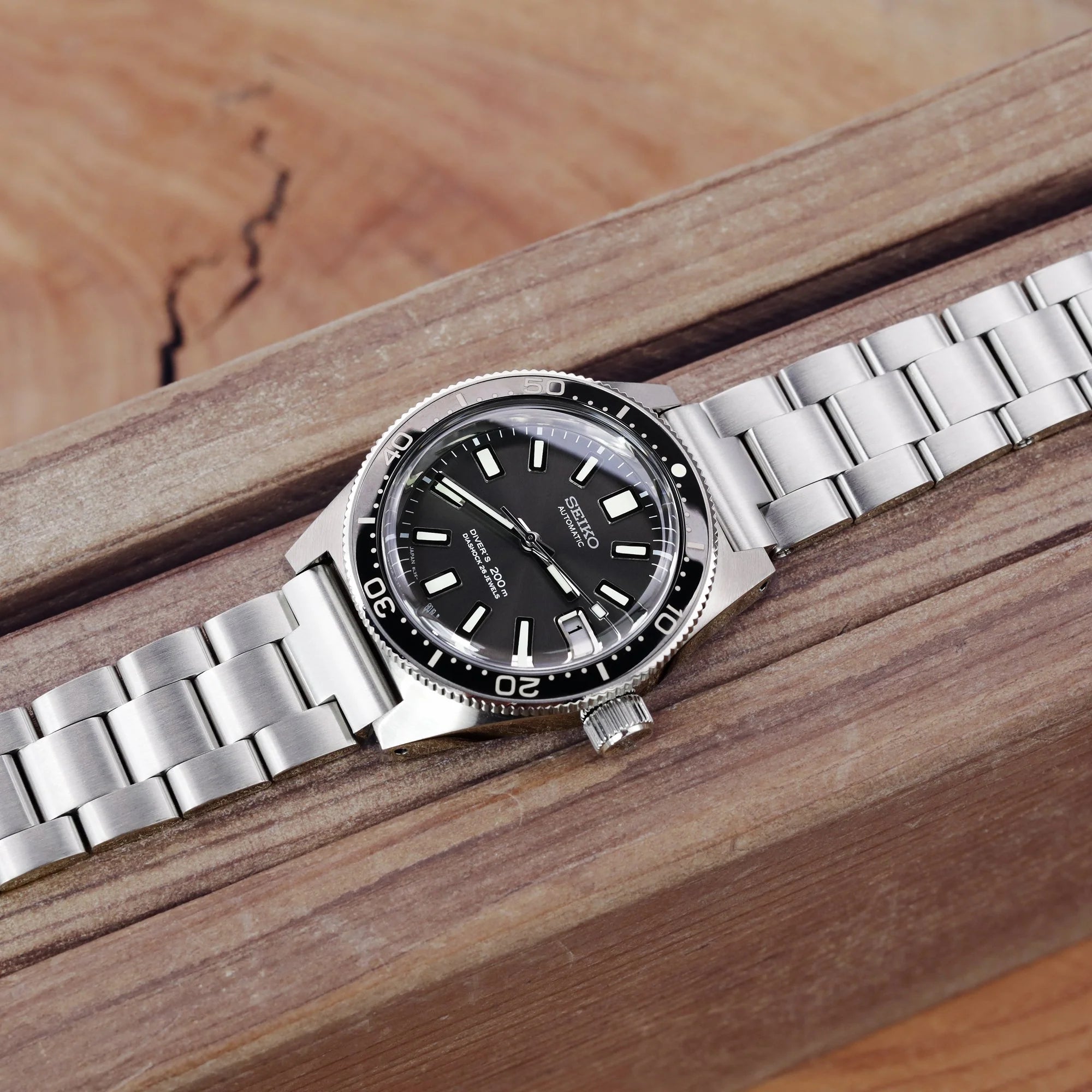 Stainless steel dive watch with black dial and bezel on brushed 316L metal bracelet, displayed on wooden surface