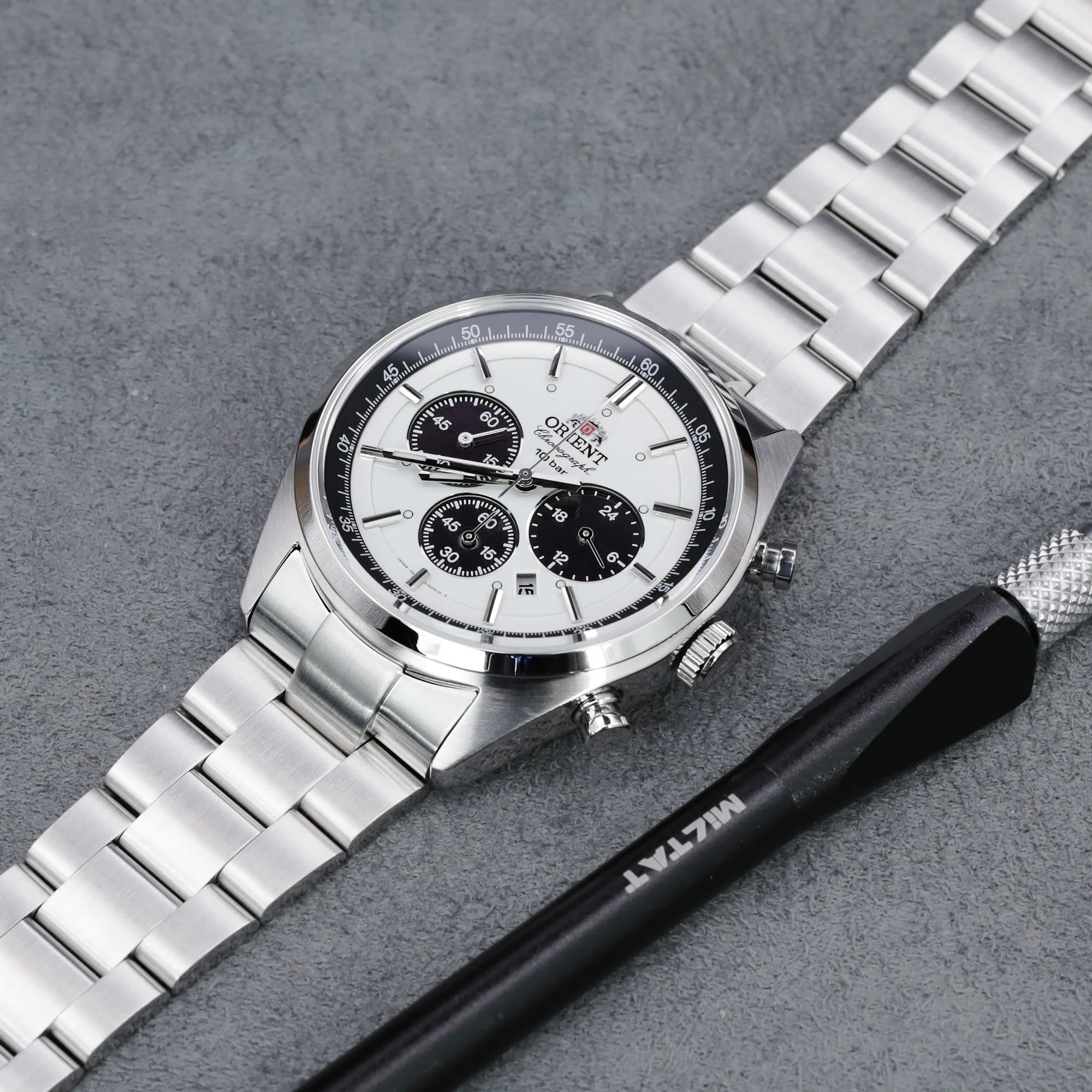 Silver stainless steel bracelet watch with white dial, chronograph subdials, and metal band on gray surface with black tool