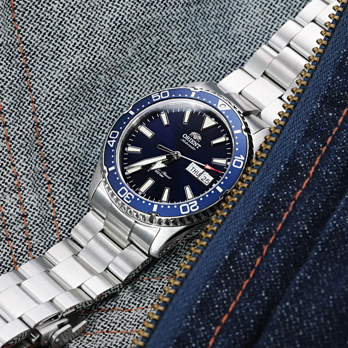Orient Kamasu automatic dive watch with blue bezel and stainless steel bracelet on fabric background