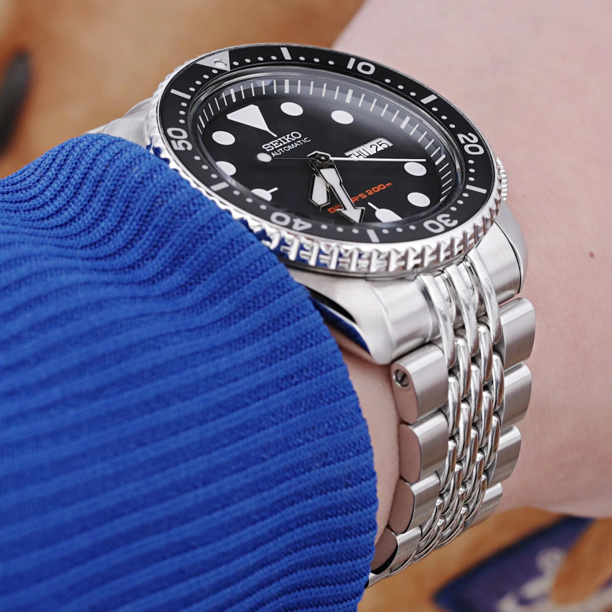 Seiko SKX007 automatic dive watch with stainless steel Goma BOR bracelet worn on blue sleeve, black dial with white indices
