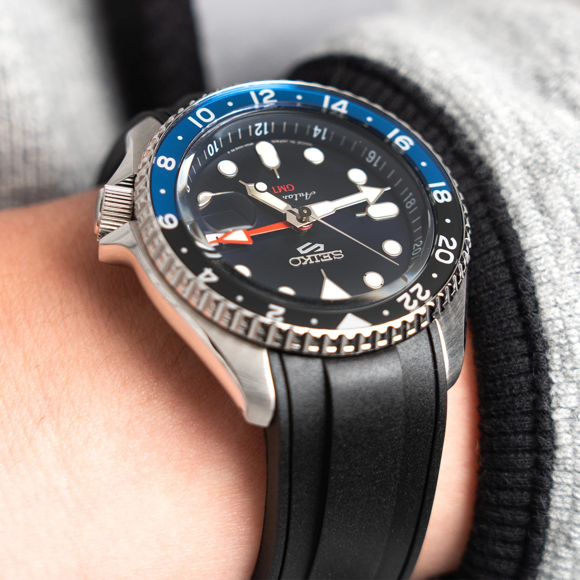 Black rubber curved-end watch strap for Seiko 5 Sports on wrist with blue bezel dive watch
