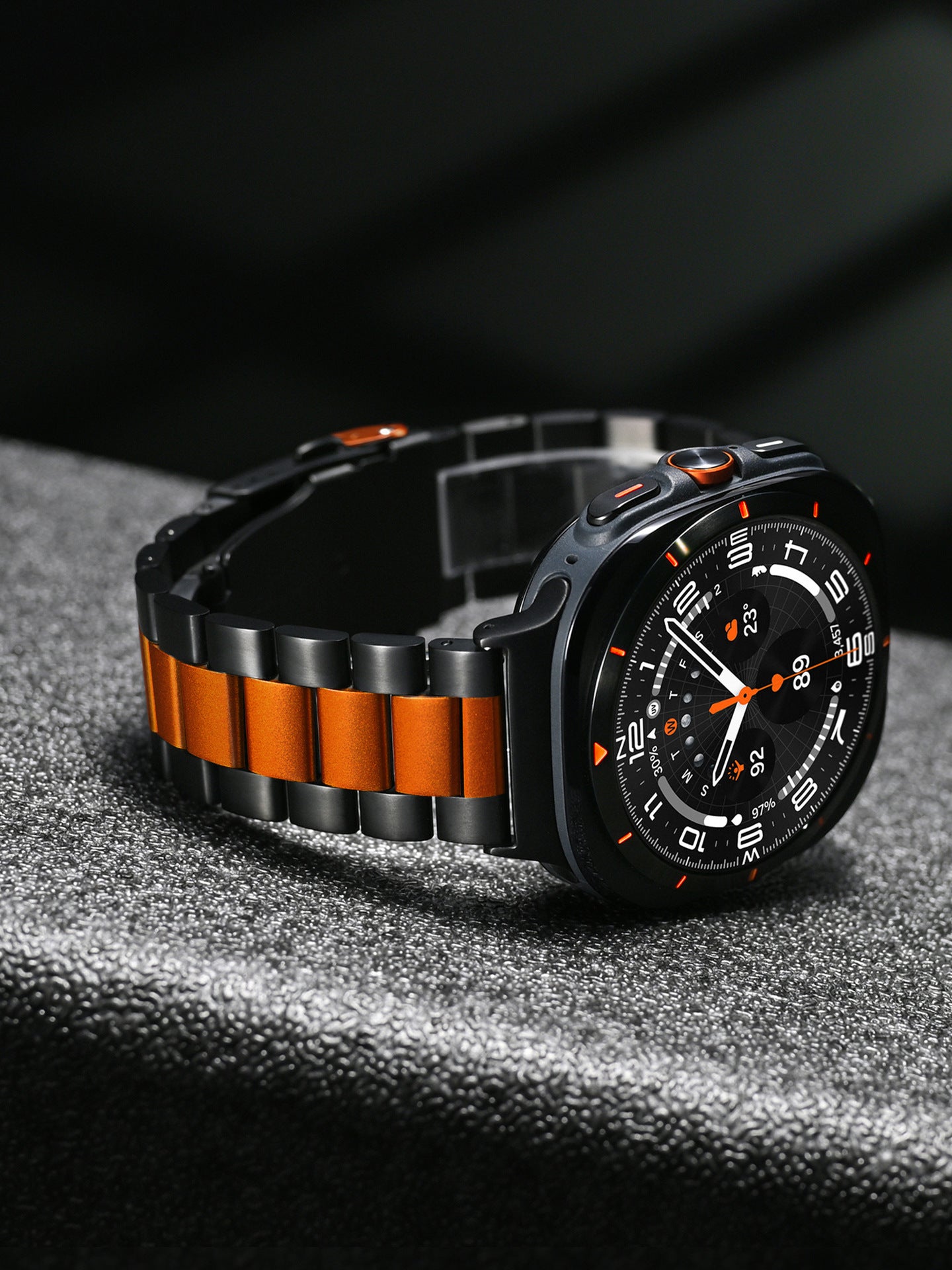 Black and orange sports watch with steel bracelet, chronograph dial, and orange accents on textured surface
