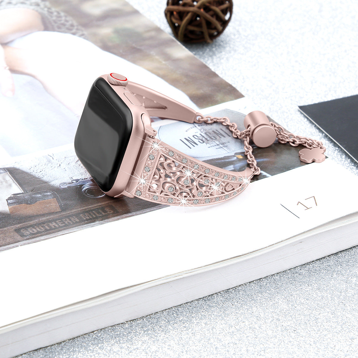 Rose gold decorative smartwatch band with ornate filigree pattern and crystal embellishments, featuring charm detail on pink Apple Watch