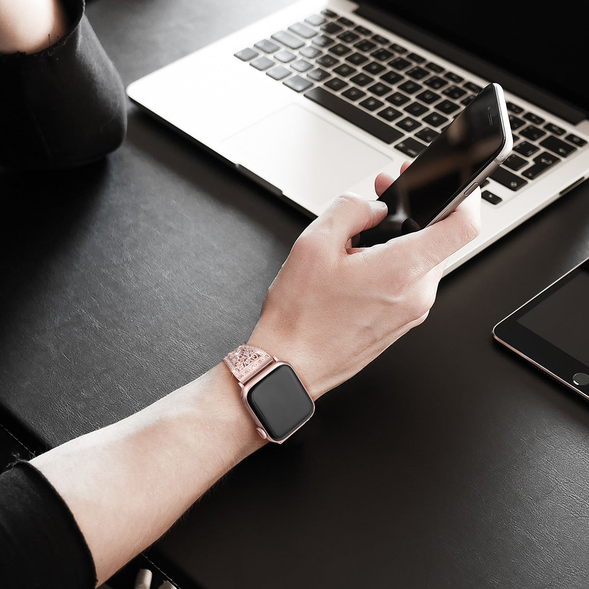 Woman wearing rose pink glitter smartwatch band while holding smartphone at laptop desk workspace