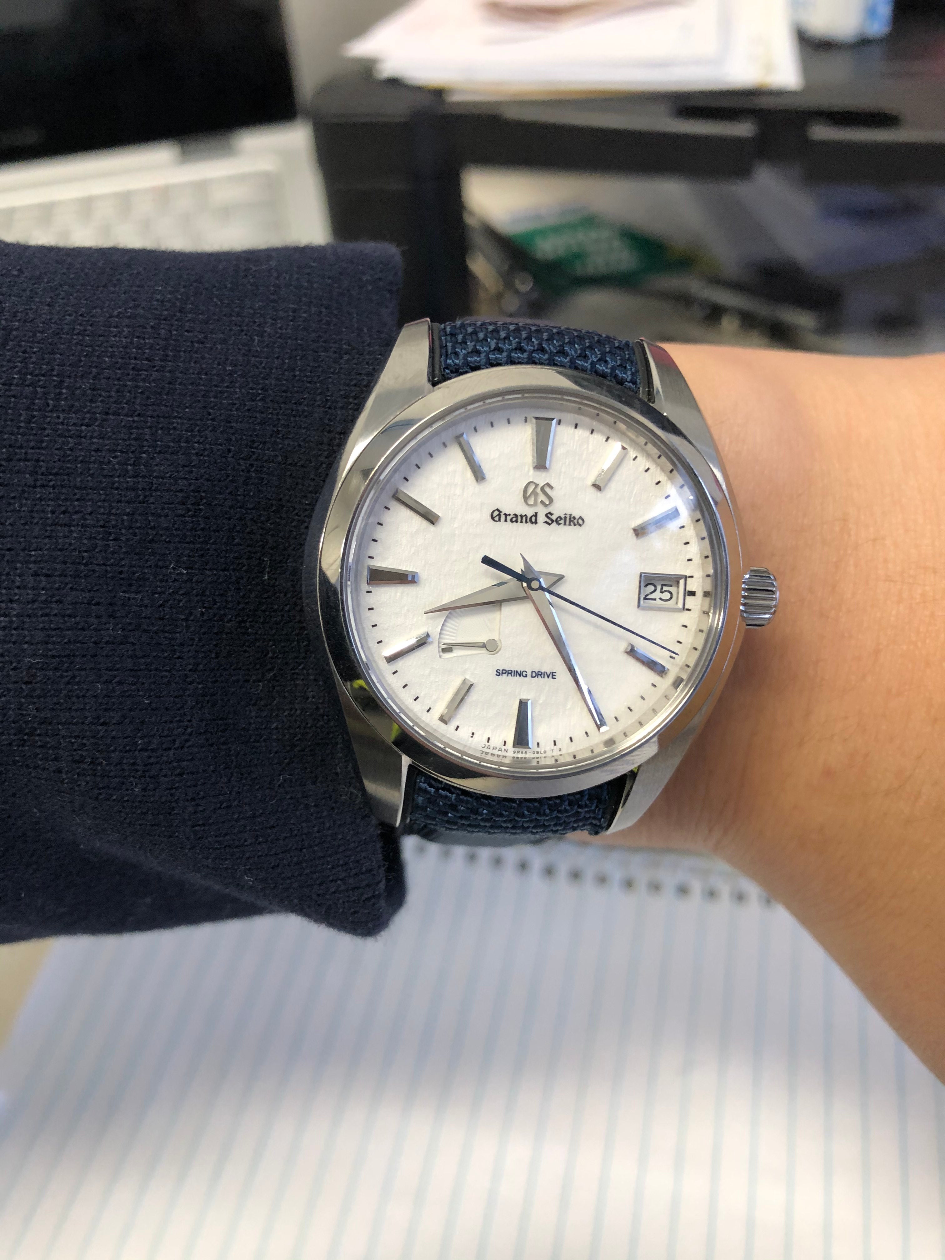 Grand Seiko Spring Drive watch with silver case, cream dial, date window, and navy blue fabric strap worn on wrist