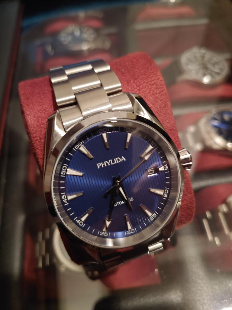 Phvlida stainless steel watch with blue dial on red display cushion, metal bracelet visible