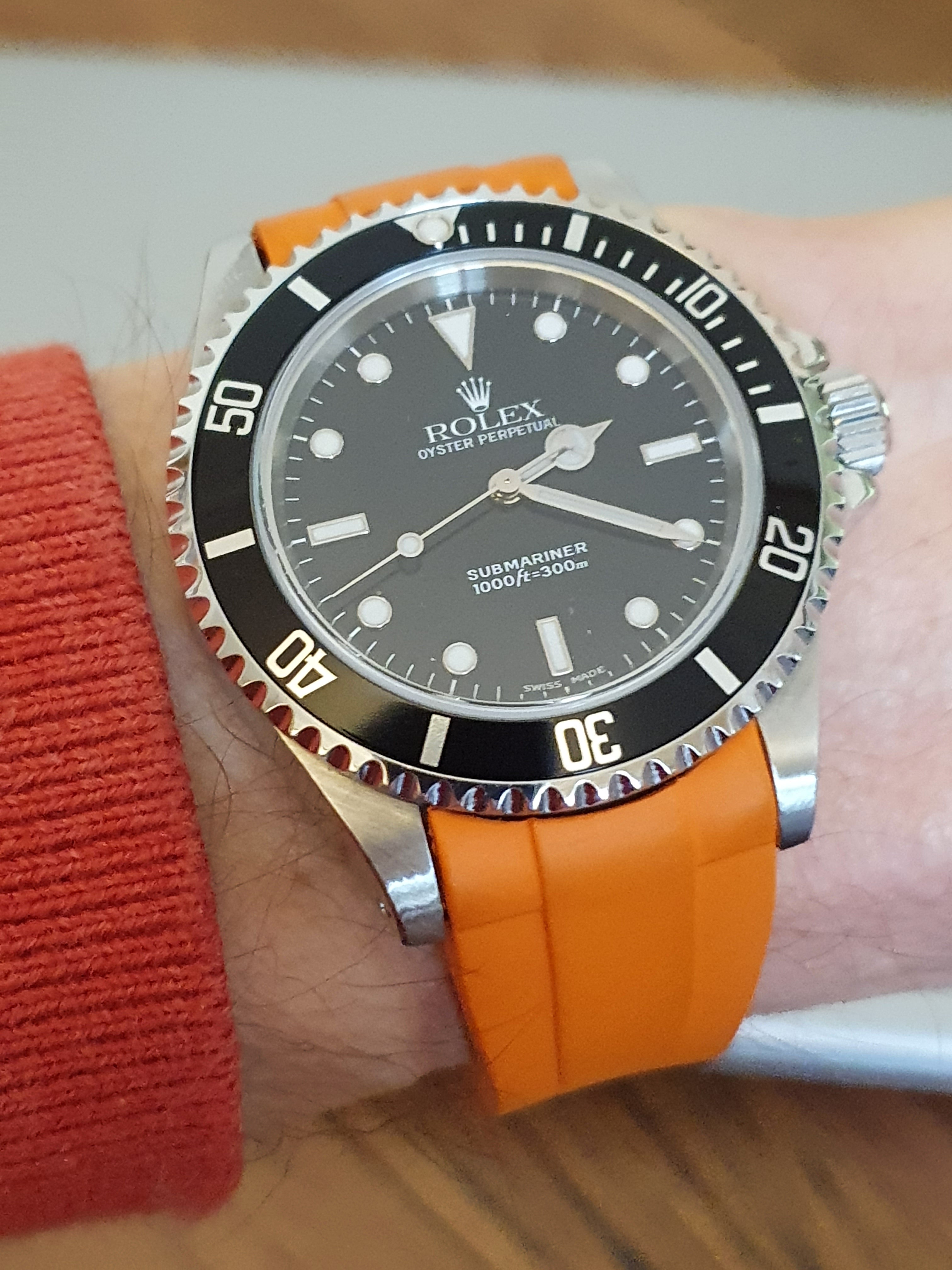 Rolex Oyster Perpetual Submariner dive watch with black dial, black bezel, orange rubber strap on wrist