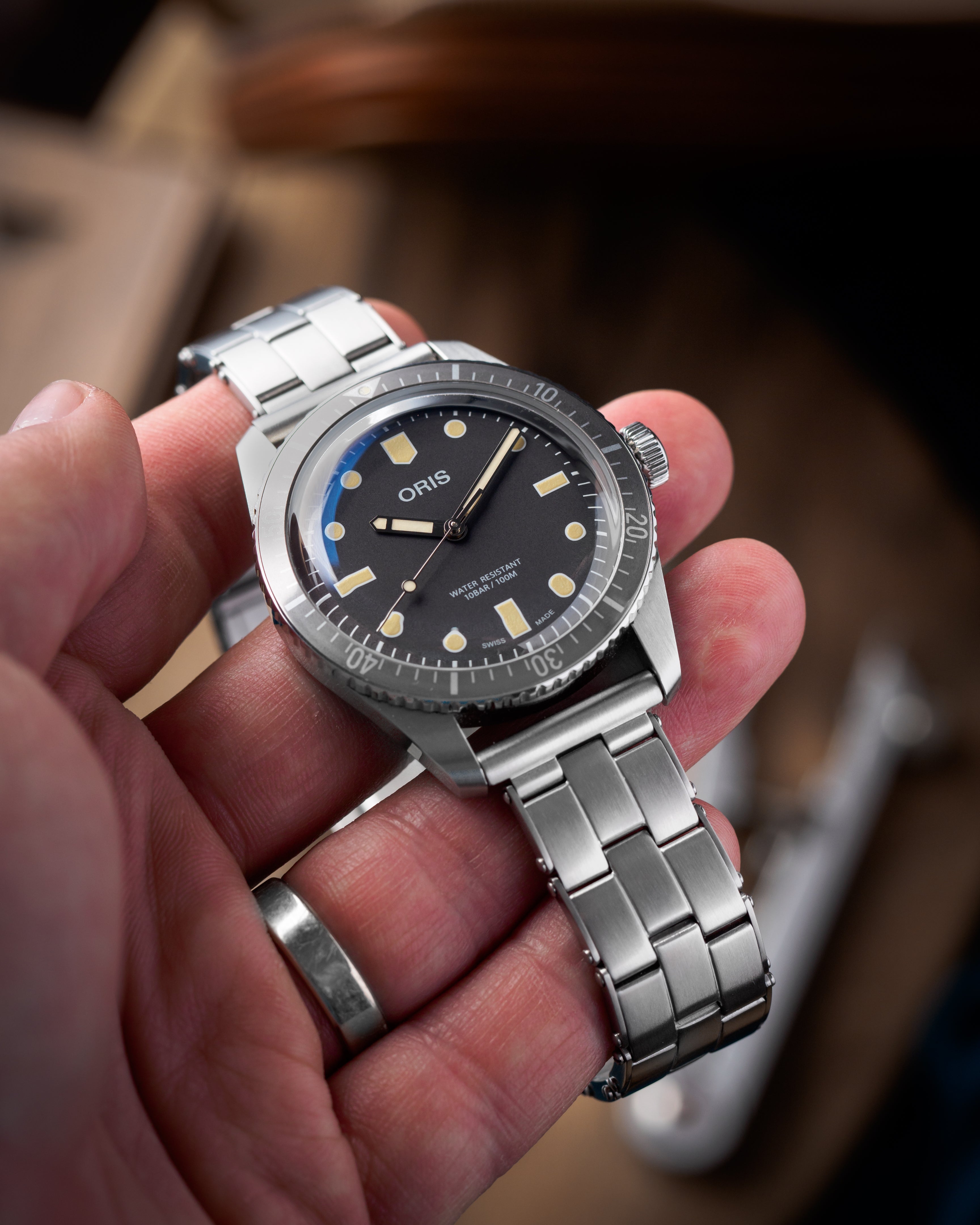 Oris stainless steel dive watch with black dial, applied indices, and matching metal bracelet held in hand