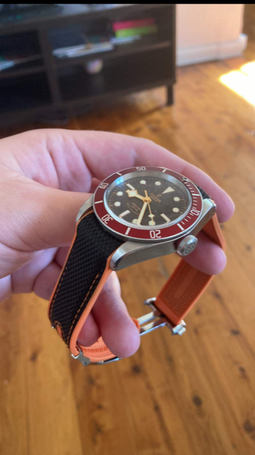Curved King hybrid rubber watch strap in black and orange with deployant clasp, displayed on wrist in home setting