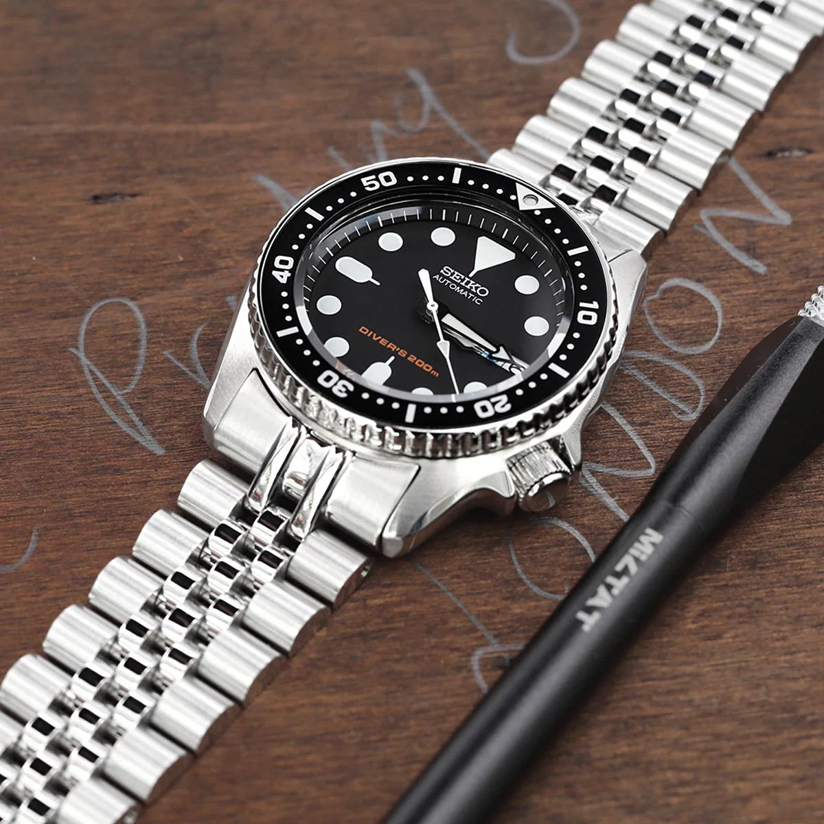 Seiko SKX013 dive watch with black dial and luminous hour markers on stainless steel Super-J Louis bracelet, displayed on wooden surface