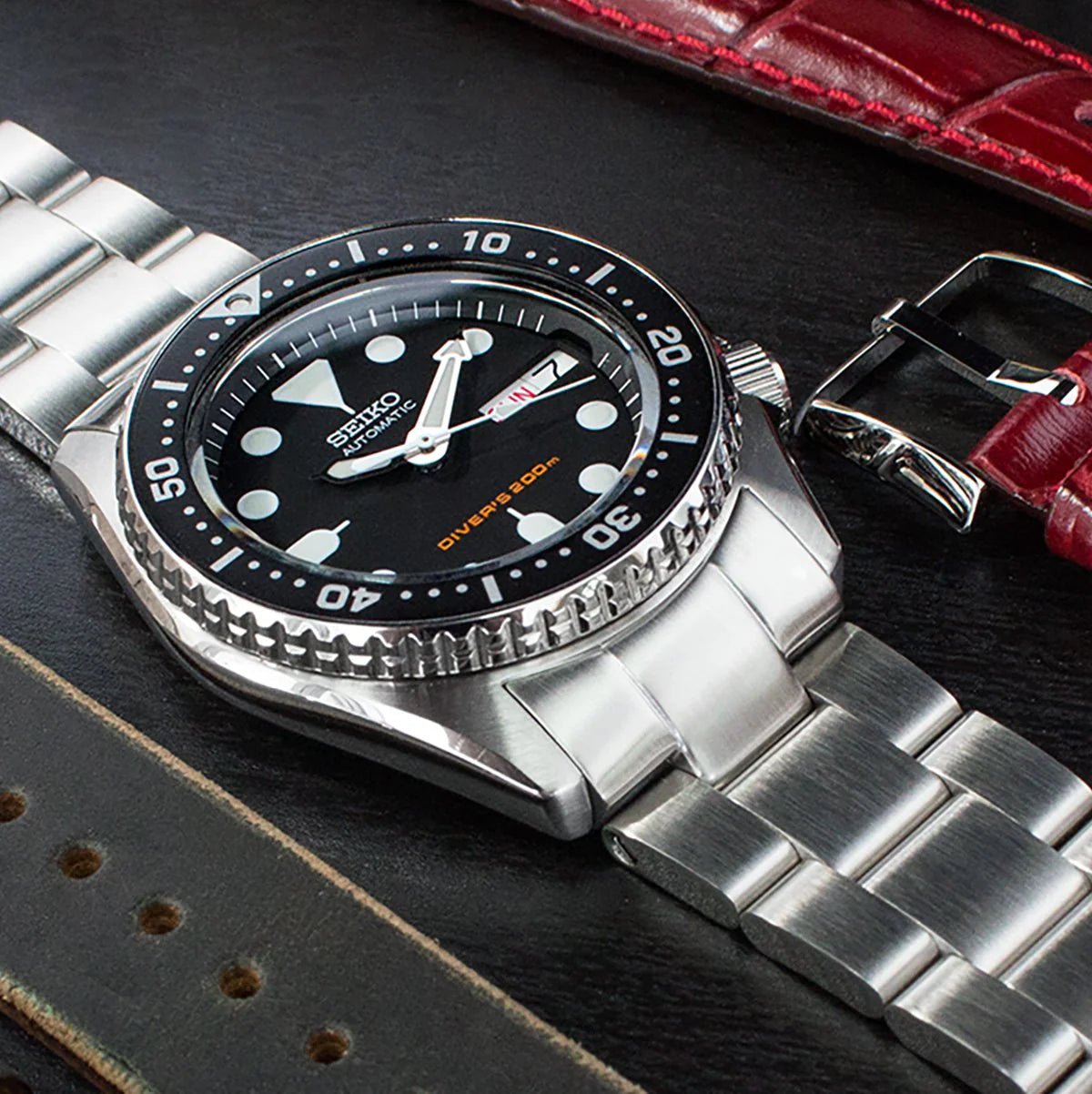Seiko SKX013 dive watch with stainless steel Super-O Boyer bracelet on black leather strap background