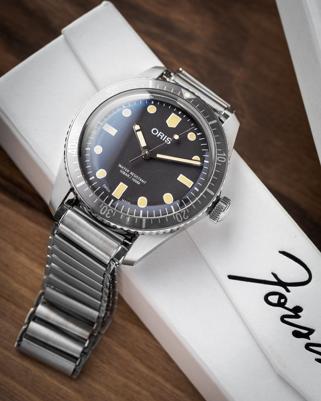 Oris dive watch with black dial, luminous hour markers, stainless steel bracelet on white display stand