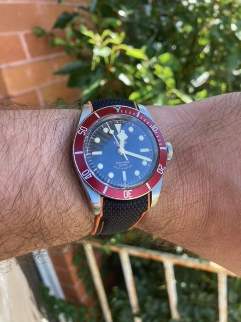 Vintage dive watch with blue dial and red bezel on black hybrid rubber strap with deployant clasp, worn on wrist outdoors