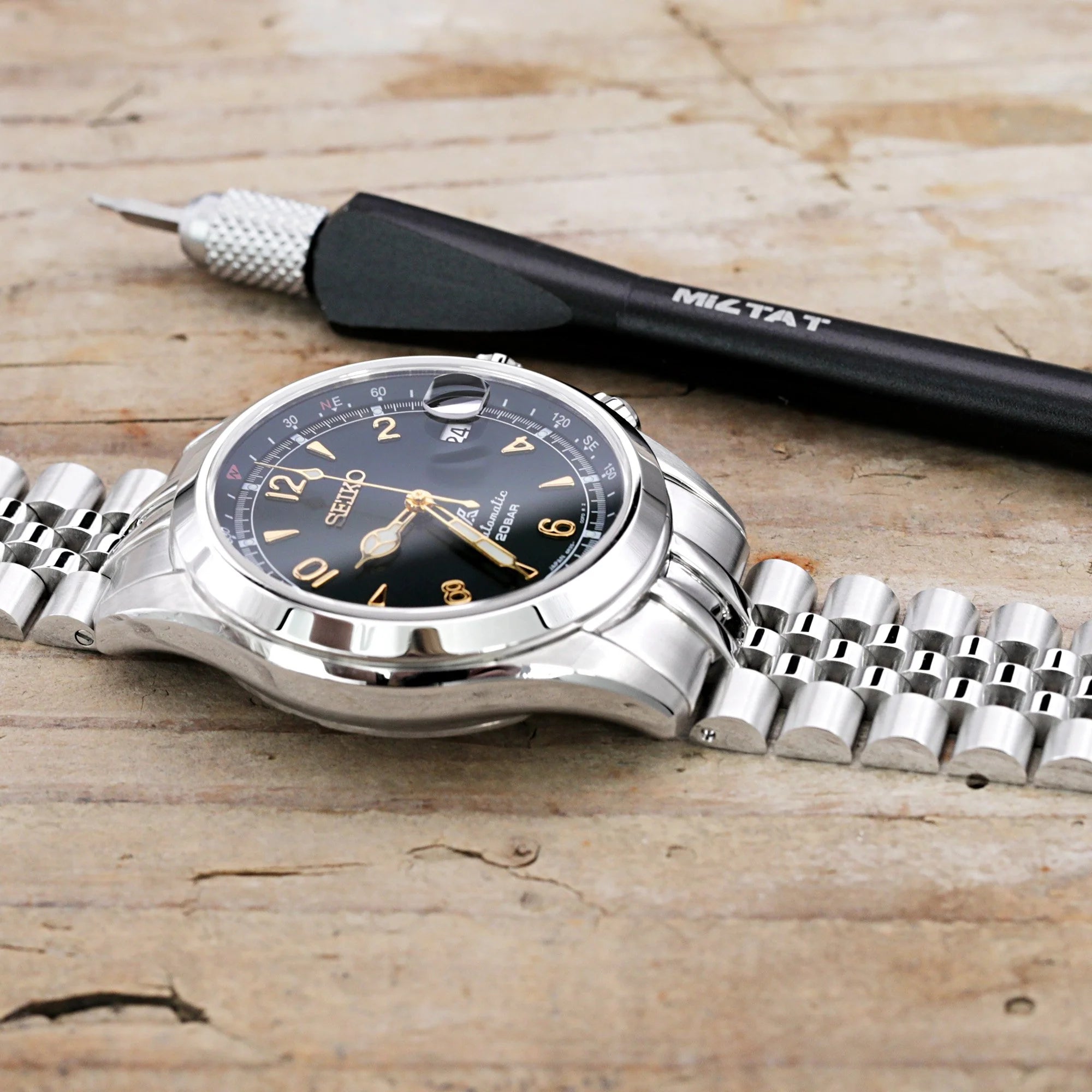 Seiko Alpinist SARB017 watch with steel Super-JUB II bracelet on wooden surface next to watch cleaning tool