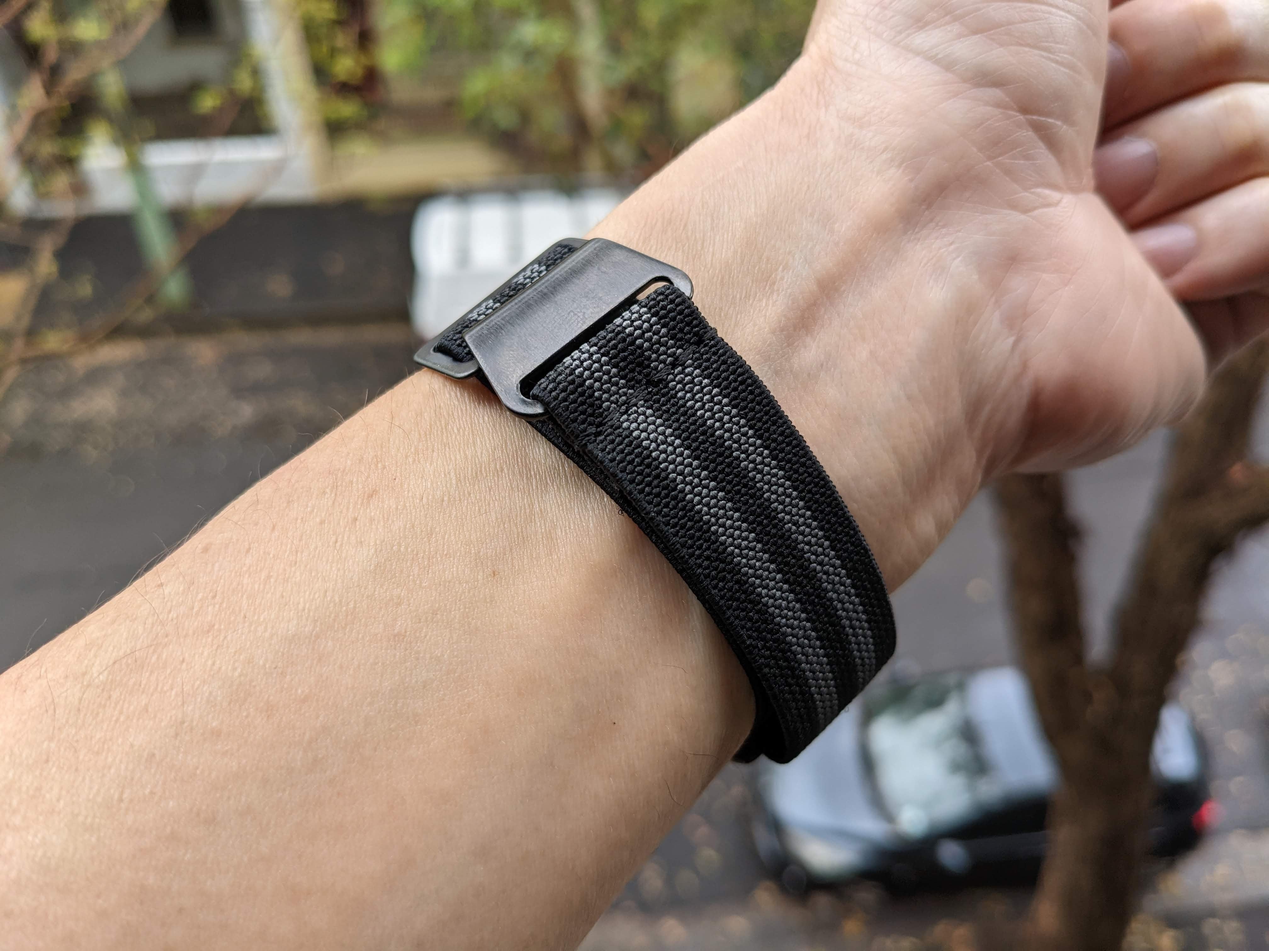 Black fabric tactical watch band with metal buckle clasp on wrist, outdoor setting