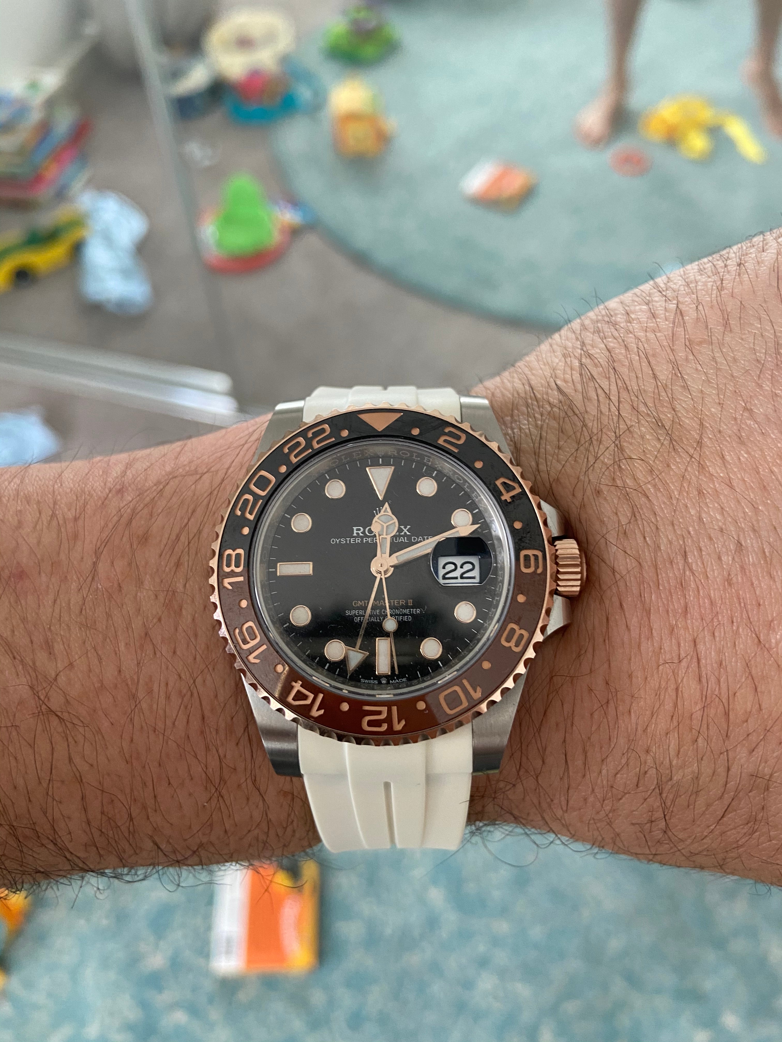 Luxury sports watch with black dial, brown and gold bezel, date window, and white rubber strap worn on wrist